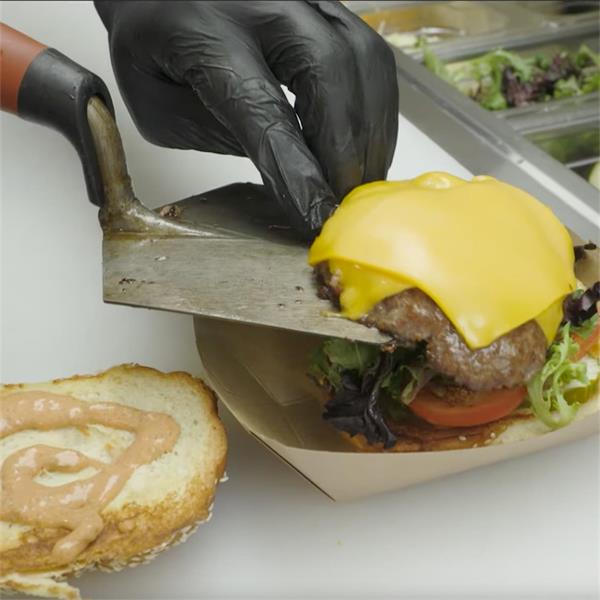 Person using a MARSHALLTOWN hamburger trowel to assemble a burger