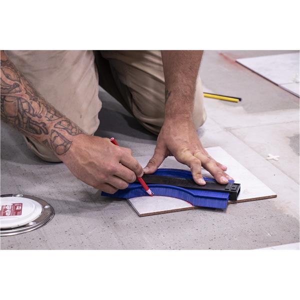 Person using a MARSHALLTOWN contour gauge to trace a shape on tile flooring