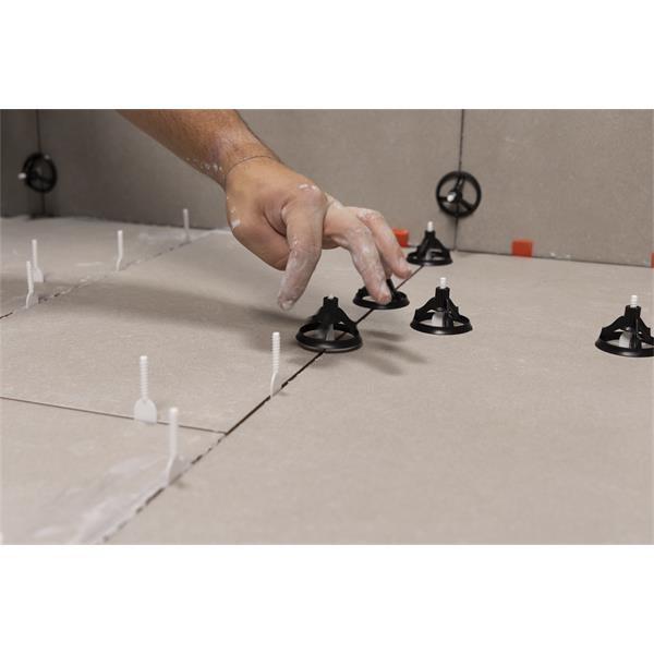 Hand placing a BARWALT PLS Revolve Tile Leveling System on floor tiles